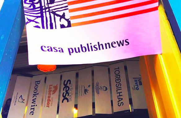 Flâmula na frente da Casa PublishNews e os banners de seus parceiros ao fundo | © Mariana Bueno