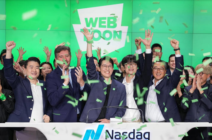 Ao centro, o CEO da Webtoon, Junkoo Kim, na abertura do pregão da Nasdaq no dia 27 | © Webtoon Entertainment Ao centro, o CEO da Webtoon, Junkoo Kim, na abertura do pregão da Nasdaq no dia 27 | © Webtoon Entertainment